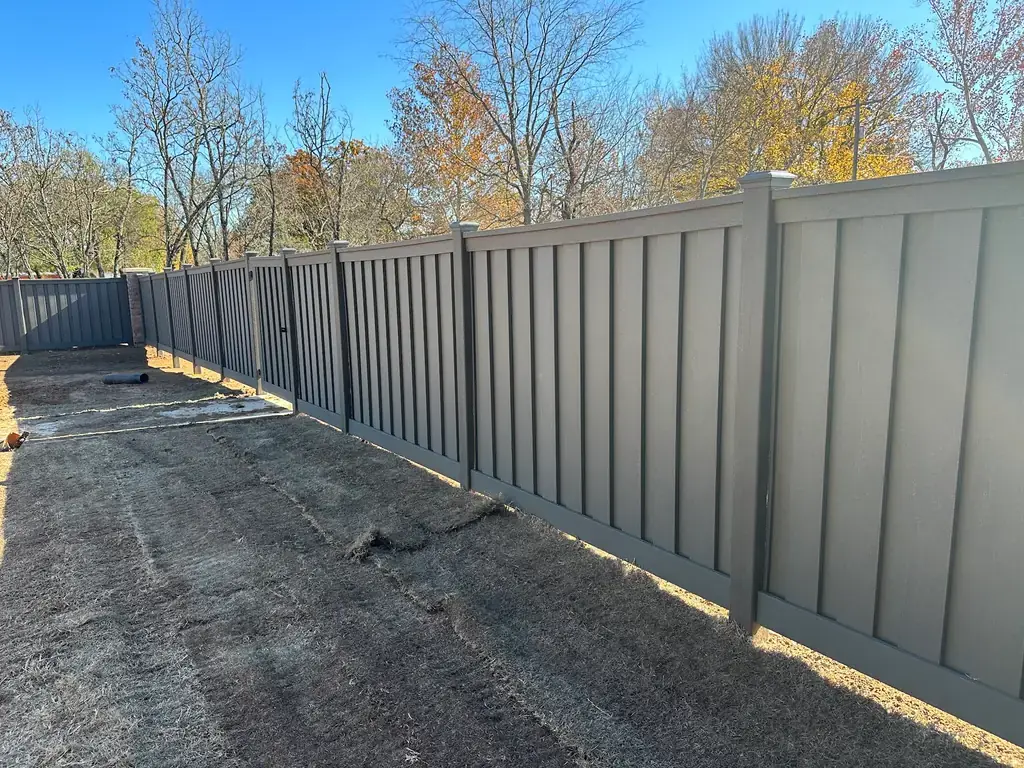 A long run of taupe composite privacy fence set against an autumn treeline